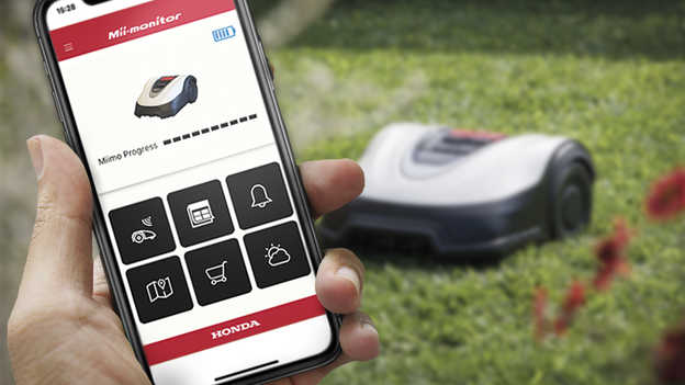 Aplikácia Mii-montor v telefóne s kosačkou Miimo pracujúcou na trávniku v pozadí.