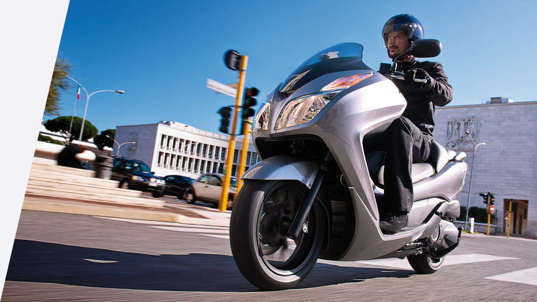 Predný trojštvrťový pohľad na model Honda Forza 300 s jazdcom. Pohľad zľava (na ceste).