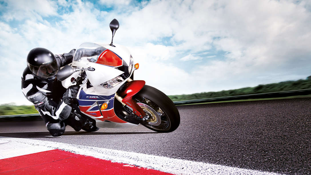 Predný 3/4 pohľad na motocykel Honda CBR600RR s jazdcom nakloneným v zákrute. Sprava (pretekársky okruh).