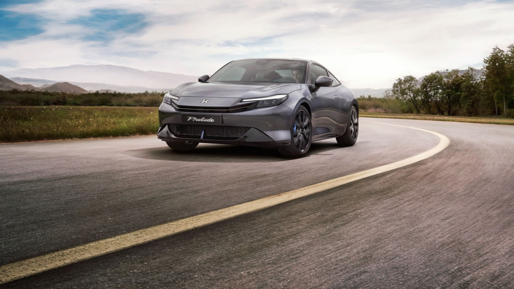 Honda Prelude vo farbe Crystal Black Pearl jazdiaca po kľukatej ceste s voľnou krajinou v pozadí.