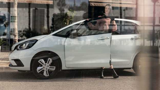 Bočný pohľad na zaparkovaný model Honda Jazz a na ženu otvárajúcu dvere