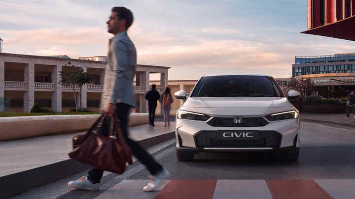 Honda Civic Hybrid sa blíži k mužovi pred priechodom pre chodcov.