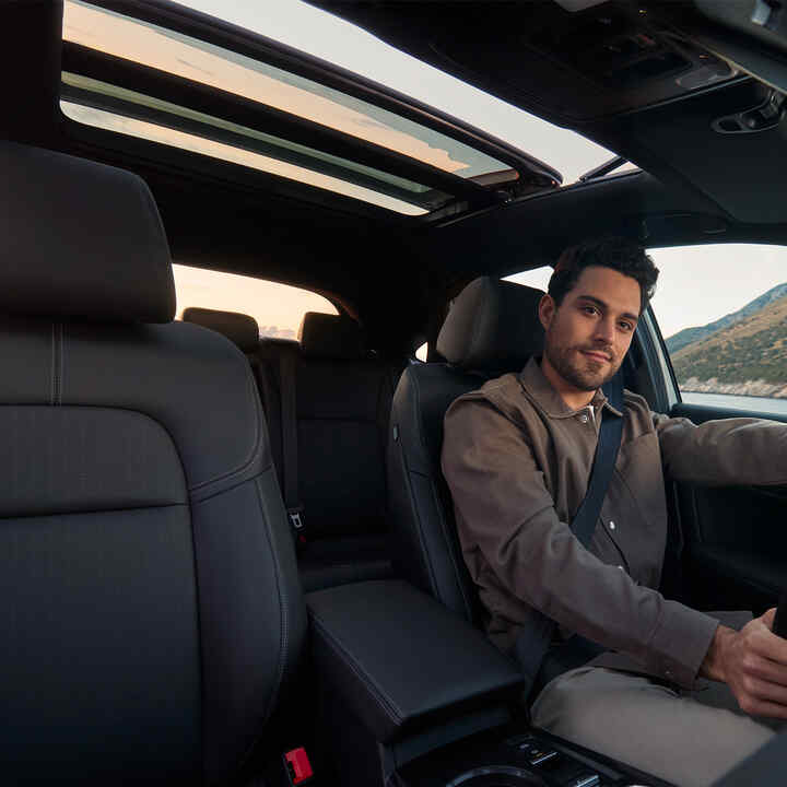 Záber interiéru vozidla Civic Hybrid s mužom za volantom, zameraný na otvorenú panoramatickú strechu.