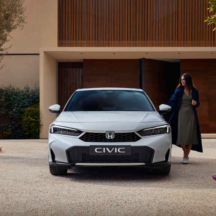 Predný pohľad na Civic Hybrid so ženou otvárajúcou dvere.