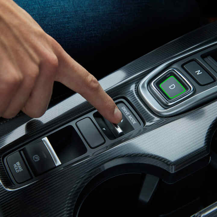 Detailný záber na osobu, ktorá prepína režimy jazdy vo vnútri Civicu Hybrid.