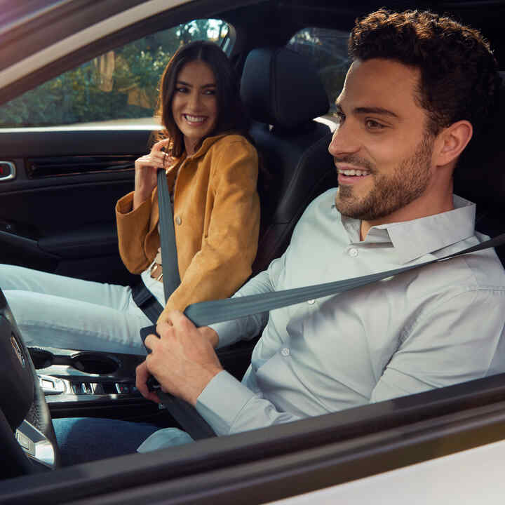 Dvaja ľudia sediaci v prednej časti vozidla Honda Civic Hybrid a zapínajúci si bezpečnostné pásy.