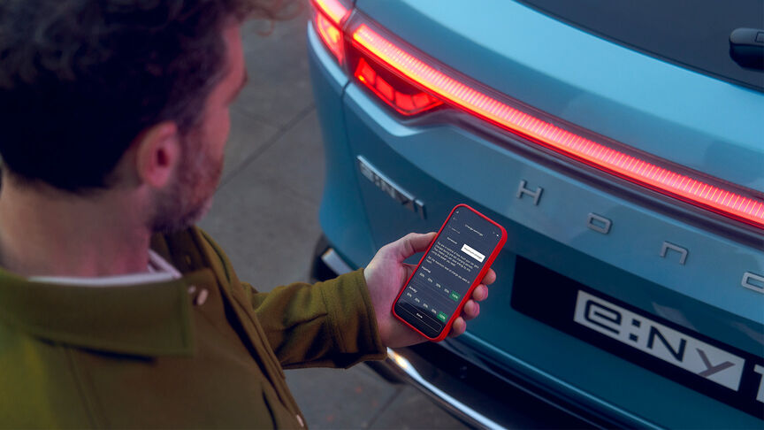 Dáma stojaca vedľa bieleho vozidla Honda e používajúca aplikáciu My Honda Plus