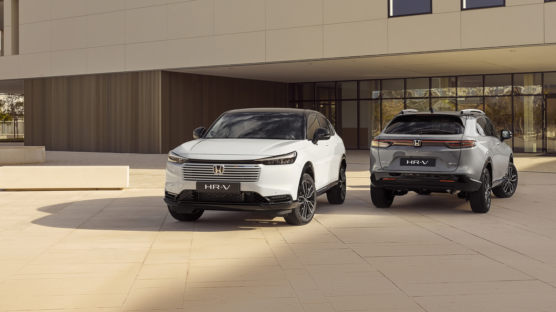 Two Honda HR-V SUVs parked outside a modern building, shown from front and rear angles—one in white facing forward and one in silver facing away.