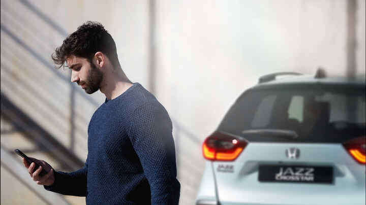 Osoba pozerajúca sa na smartfón, v pozadí Honda Jazz Crosstar.