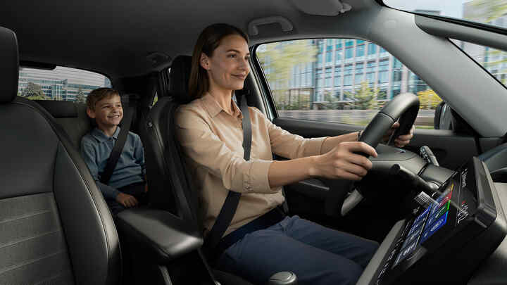 Žena šoférujúca Hondu Jazz Hybrid s dieťaťom na zadných sedadlách.