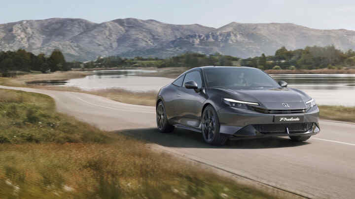 Bočný profil vozidla Honda Prelude Hybrid jazdiaceho popri jazere so sviežimi zelenými stromami.