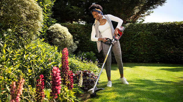 Žena používa akumulátorový vyžínač Honda na tráve v záhrade a predstavuje ochranu rastlín.
