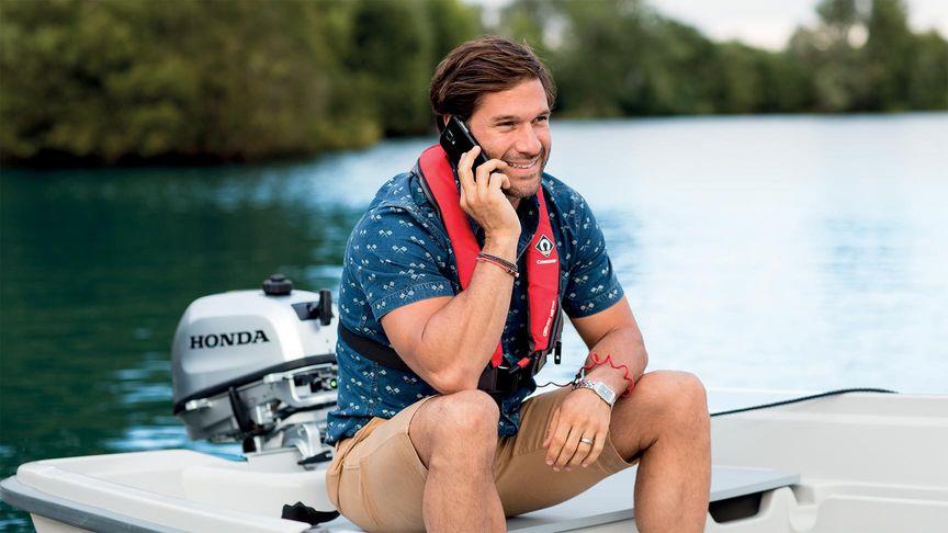 Muž na malom člne telefonuje a nabíja mobilný telefón pomocou závesného motora Honda