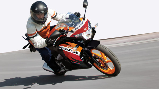 Honda CBR125R motorcycle front-threequarter view with rider, leaning into bend. Right-facing (Road location).