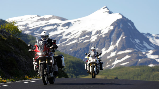 Dva motocykle idúce po ceste so zasneženými horami v diaľke.