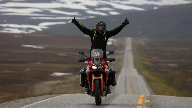 Muž na motocykli Honda Africa Twin so zdvihnutými rukami na cestách v Nordkappe.