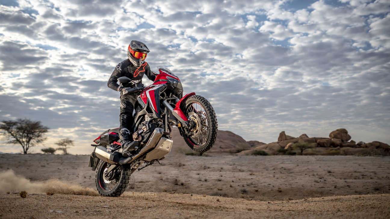 Trojštvrťový pohľad spredu z pravej strany na model Honda Africa Twin pri jazde so zdvihnutým predným kolesom v púšti