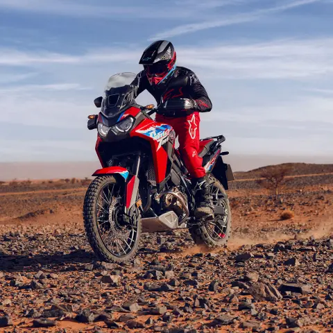 Figurant idúci na motocykli CRF1100L Africa Twin skalnatým terénom v púšti.