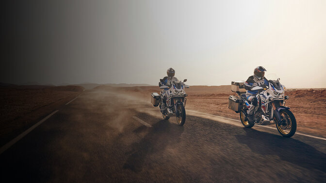 Predný trojštvrťový pohľad na jazdcov na strojoch CRF1100 Africa Twin Adventure Sports na ceste v púšti. 