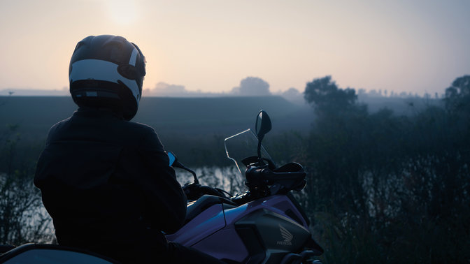 Jazdec sediaci na modeli Honda NC750X zaparkovanom vo vidieckom prostredí.