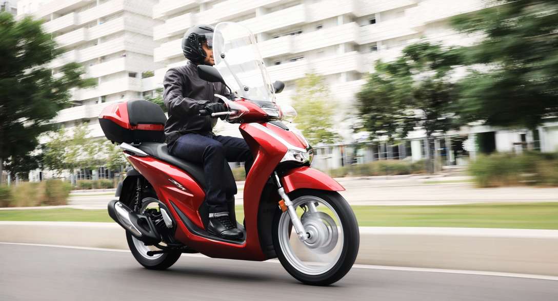 Honda SH125i, trojštvrťový pohľad spredu z pravej strany s jazdcom v meste