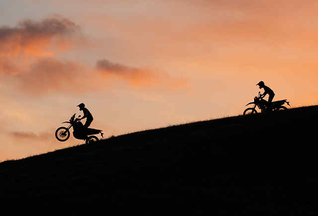 Dve motorky Hondy série 300 pri schádzaní z kopca pri západe slnka