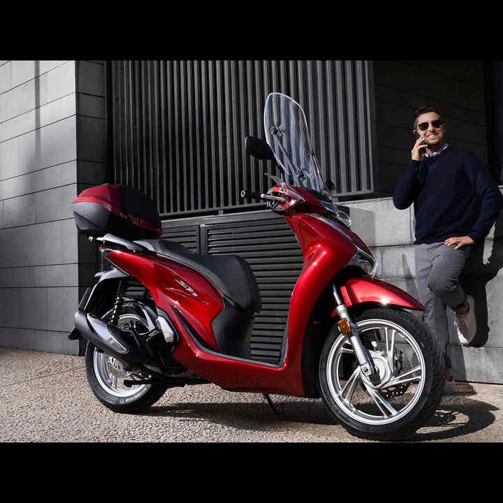 Muž s telefónom stojaci vedľa skútra Honda.