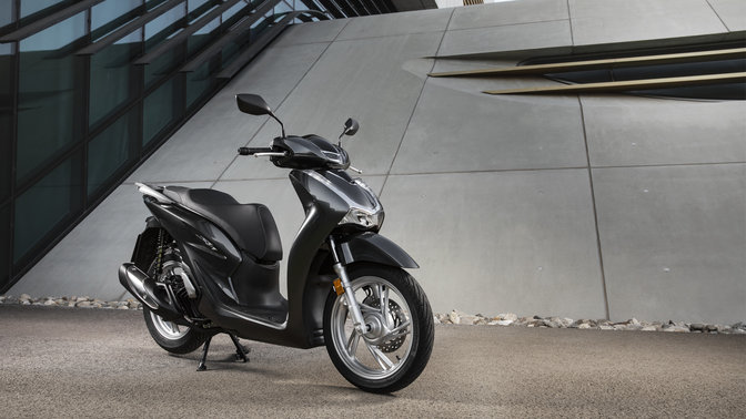 Honda Sh125i s horným kufrom a čelným štítom na ulici.