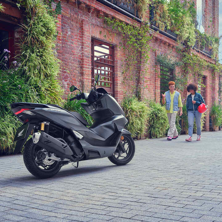 Figuranti kráčajúci ku skútru PCX125.