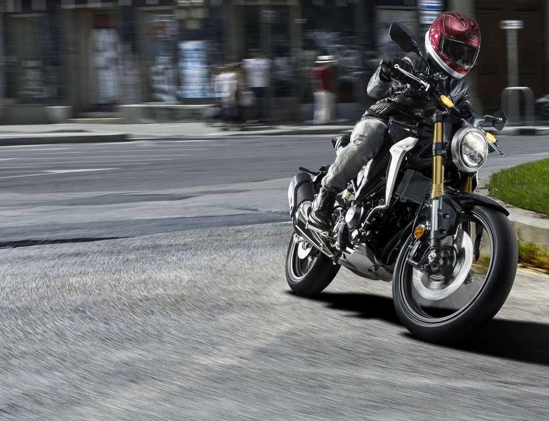 Trojštvrťový predný pohľad na motocykel Honda CB300R Neo Sports Café jazdiaci po ulici.